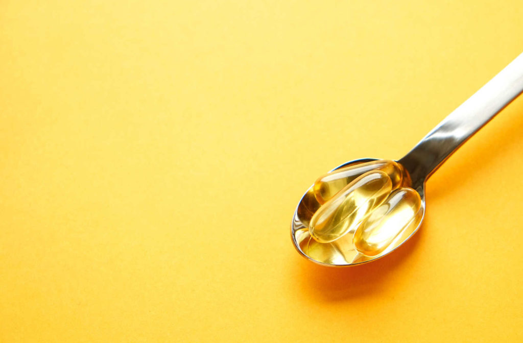 Fish oil capsules on a spoon against a yellow background.