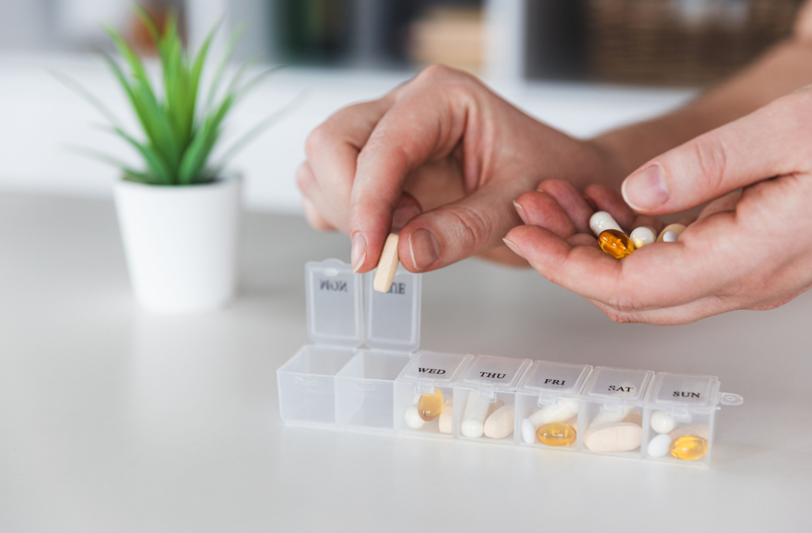 A close-up of a healthcare professional's hand as they sort pills into a plastic organizer.