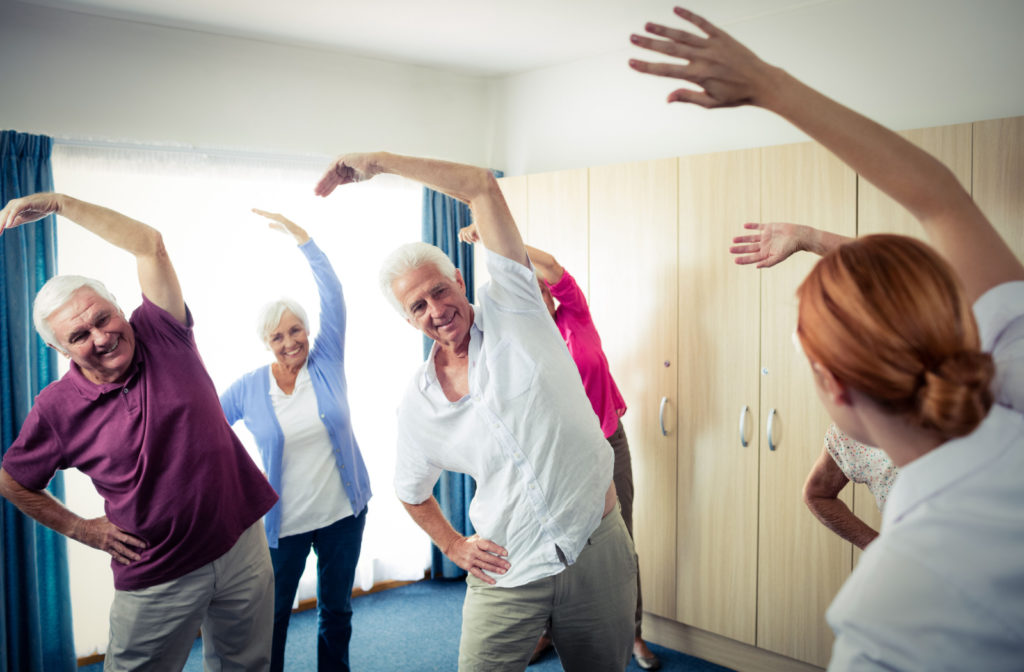A nurse stands with her back to the camera, leading a group of older adults through a series of exercises.