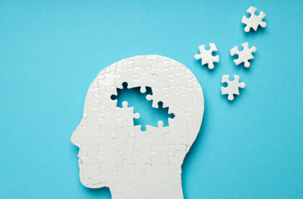 A profile of a human head puzzle on a blue background with a few pieces missing to symbolize dementia.