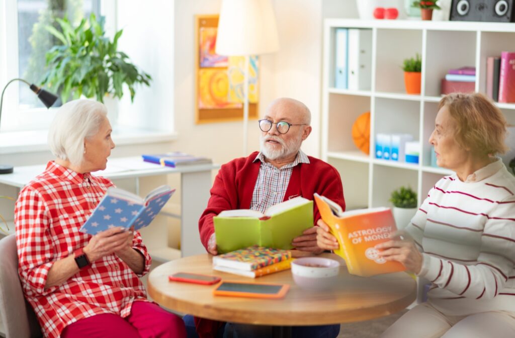Three seniors sit around a table for a book club meeting, each holding books with brightly-colored dust protectors.