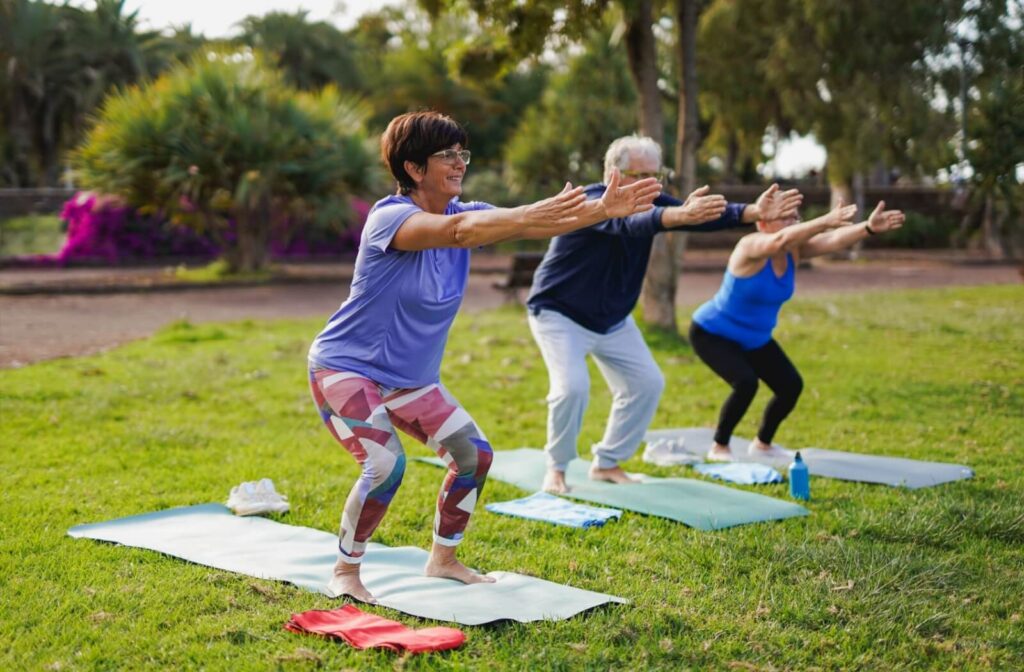 Group of older adults doing outdoor yoga on mats in a park practicing active aging and fitness