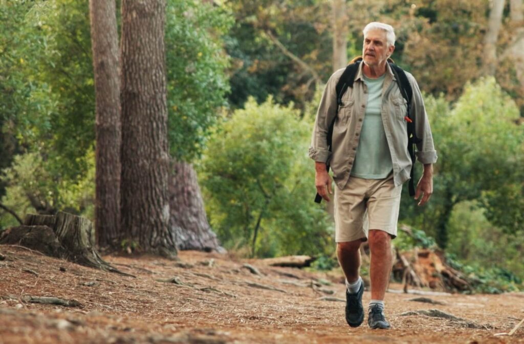Senior walking through forest trail with backpack, benefiting from outdoor activity and healthy living.