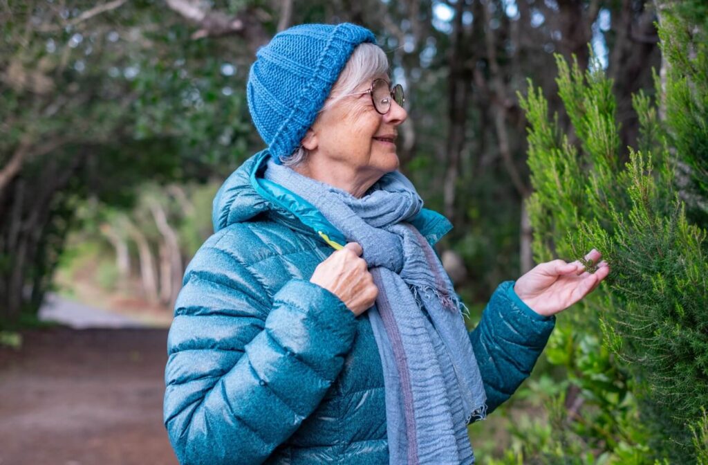 Older adult bundled in winter gear smiling while walking in wooded area enjoying nature and active aging
