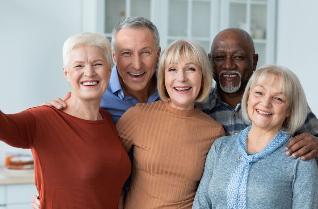A group of 5 residents in senior living smile and take a photo together while standing outside in a courtyard