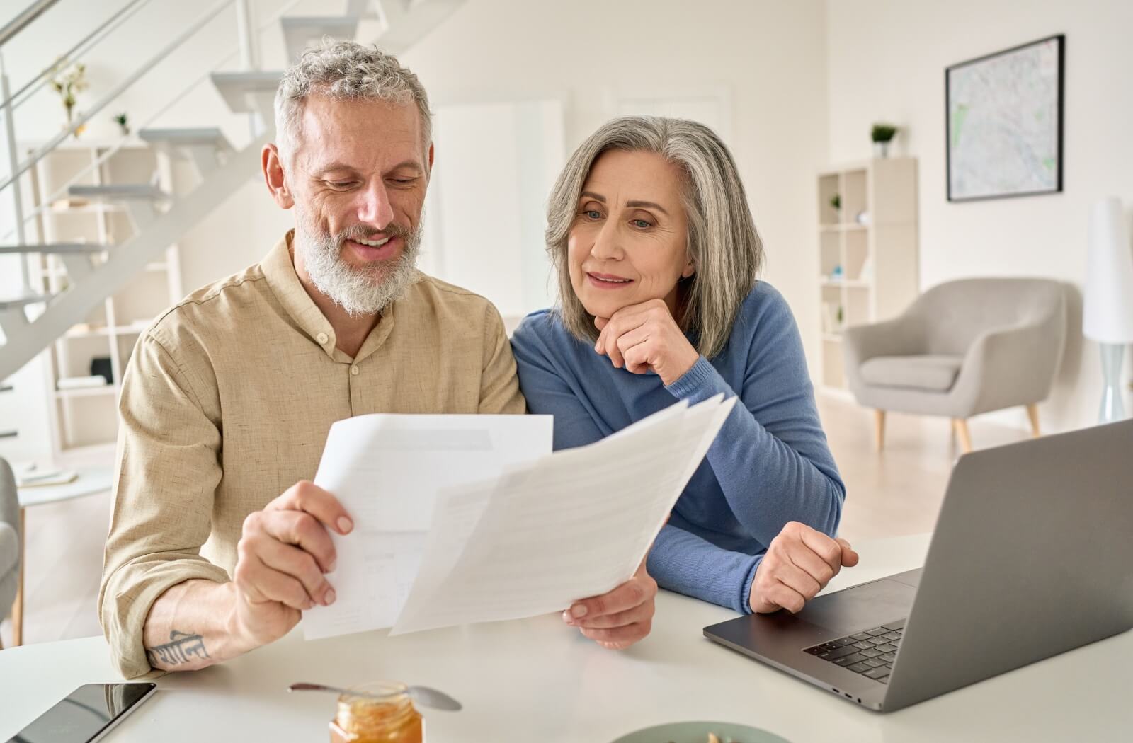 Older adults sitting at a kitchen table reviewing documents together with a laptop nearby and a calm, well-lit home background