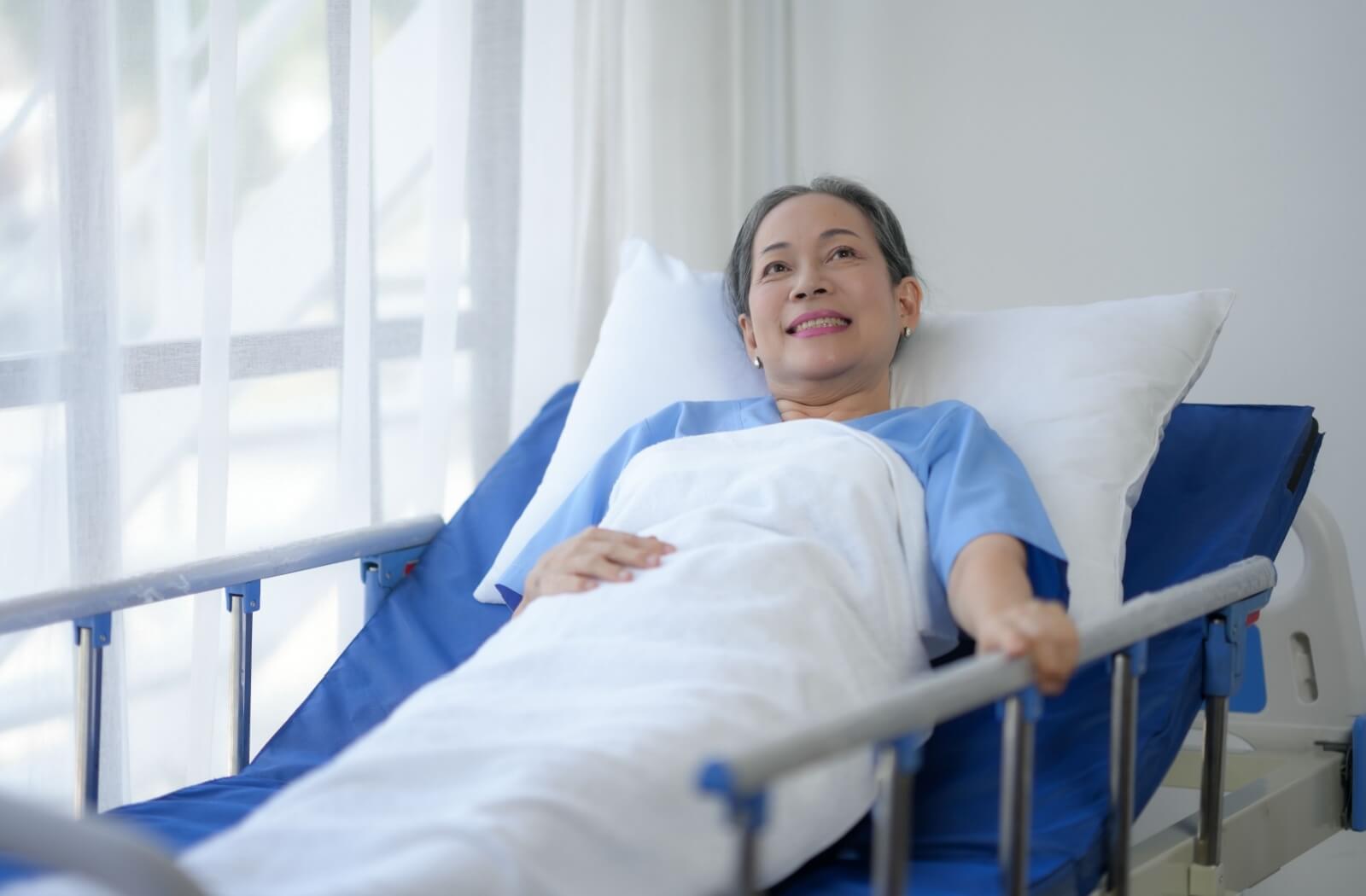 An older adult holds onto the rail of a hospital bed, ready to transition to respite care for post-surgery recovery