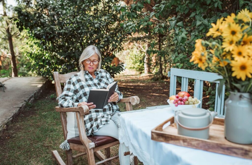 An older adult lounges in a rocking chair in the outdoors, enjoying the fresh air while reading from an exciting book
