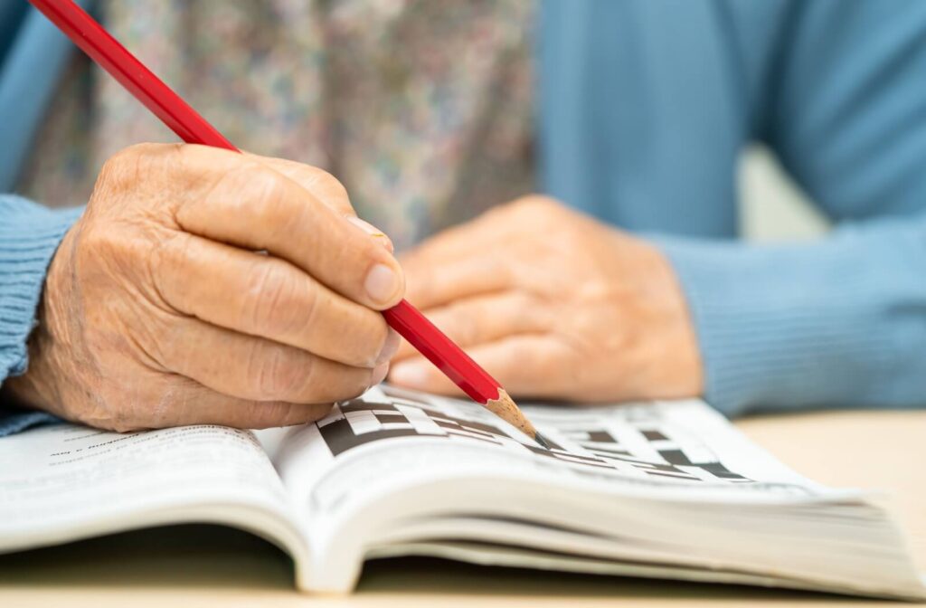 Close-up of an older adult using a red pencil to complete a physical crossword puzzle in a book